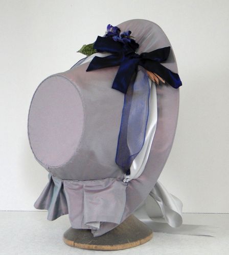 The buckram frame is covered with mauve shot taffeta and trimmed with taffeta ribbon and pansies on the right side.