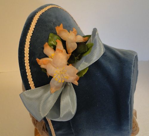 The outside is trimmed with peach coloured gimp, peach and yellow flowers, and three pale blue ribbon loops.