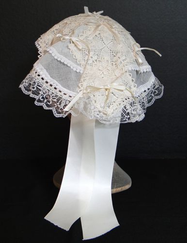 Square cotton lace motifs and small ivory satin ribbon bows trim the top layer.