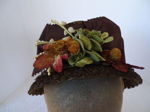 The top front edge of the crown is decorated with a triple bow of brown picot-edged ribbon, topped with hand tinted flowers.