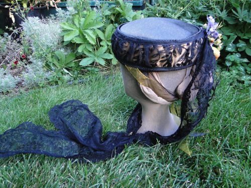 Long black lace ties come from the back of the hat to join under the chin.  Flowers trim the join and cover the snap there. Gold ribbon ties under the hair, at the back.