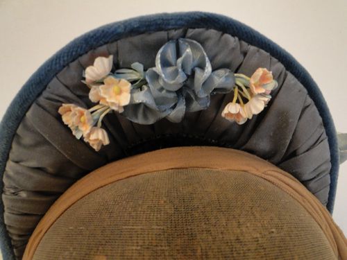 The top-inside of the brim is trimmed with peach coloured forget-me-nots and a pale blue ribbon flourish.
