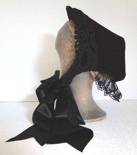 Wine velvet spoon bonnet trimmed with black lace, strings of wide black satin ribbon.  This style was worn in 1864-65.