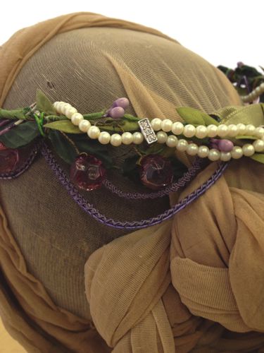 A circlet of wire was covered with green ribbon and decorated with very narrow purple gimp, purple glass beads and buds, green leaves and pearls.