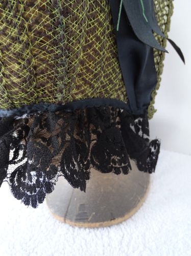 The curtain is formed by a gathered piece of black antique lace, above which is a satin ribbon that forms a protective binding of the edges of the straw.