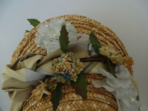 Vintage strawflowers and pale blue chiffon flowers are interspersed with dark green leaves to form the trim atop this bonnet.