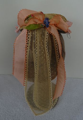 Peach posit ribbon forms a partial bow with strings.  Streamers of beige net are trimmed with off-white scallops.