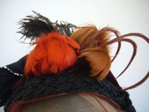 Detail view of the feather trims: two poufs of light brown and dark orange feathers, one black ostrich feather, and three brown goose biots help give the height this style requires.