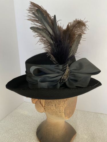 The front was trimmed with a moiré taffeta ribbon bow, metal decoration, and grey ostrich and silver rooster feathers.