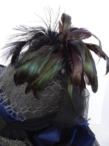 The crown was covered with draped netting, and rooster and dyed peacock feathers are added.