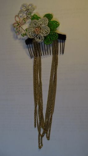 This hair comb was covered in velvet ribbon to which beaded blossoms were attached.  It was finished wilt some long strands of brass chain.